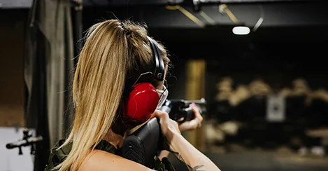 A woman wearing ear muffs and holding a gun.