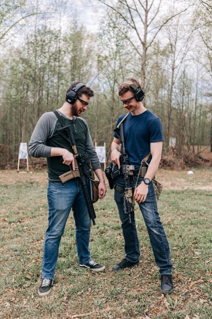 Two men standing next to each other holding guns.