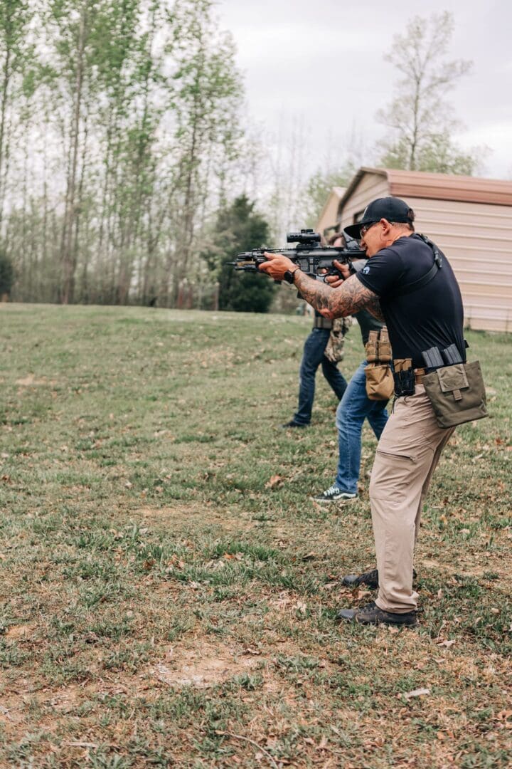 A man in black shirt holding a gun near trees.