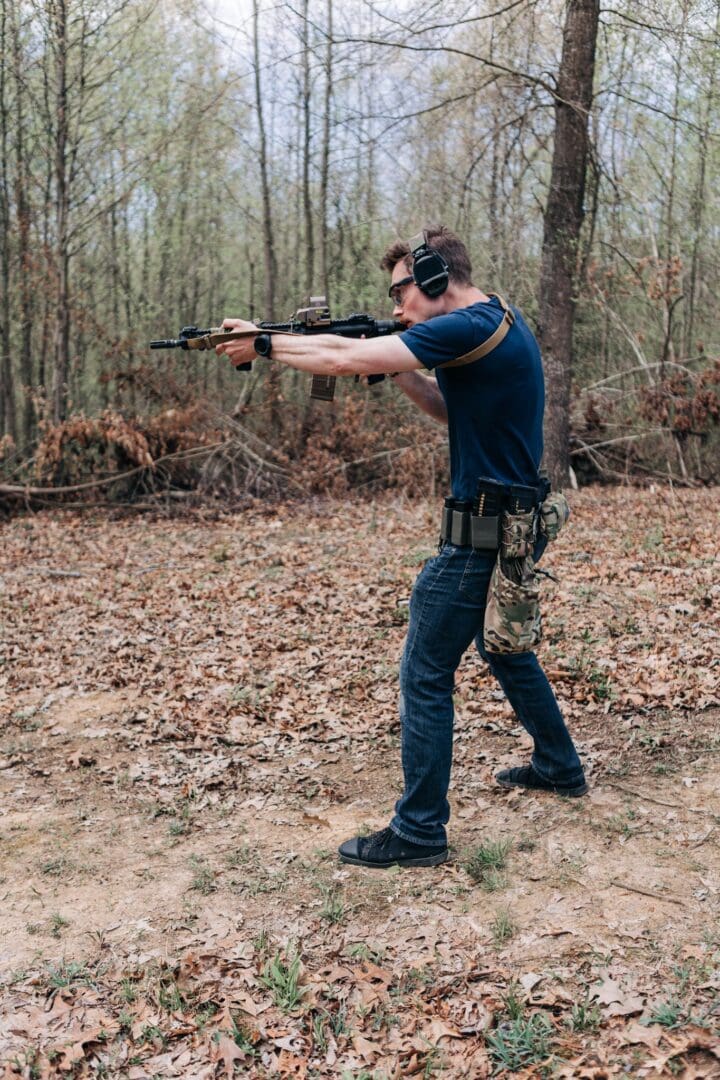 A man is holding two guns in the woods