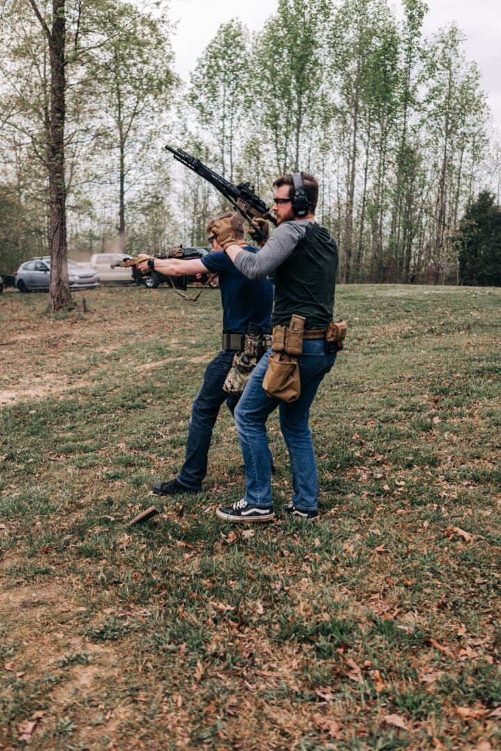 Two men are shooting guns in a field.