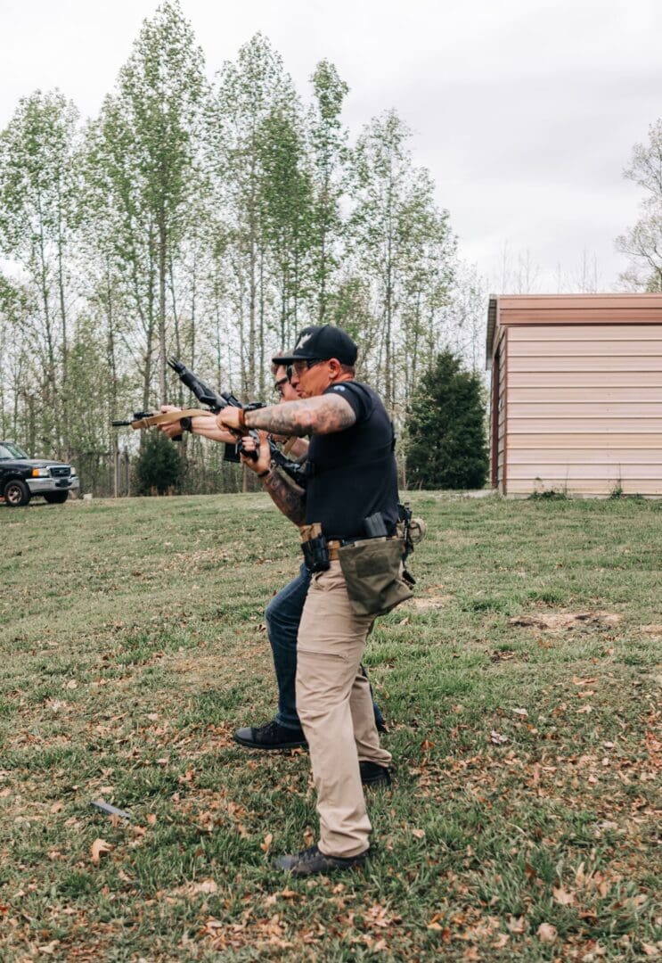 A man holding two guns while standing in the grass.