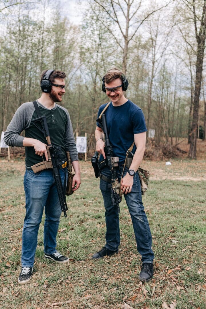 Two men standing next to each other holding guns.