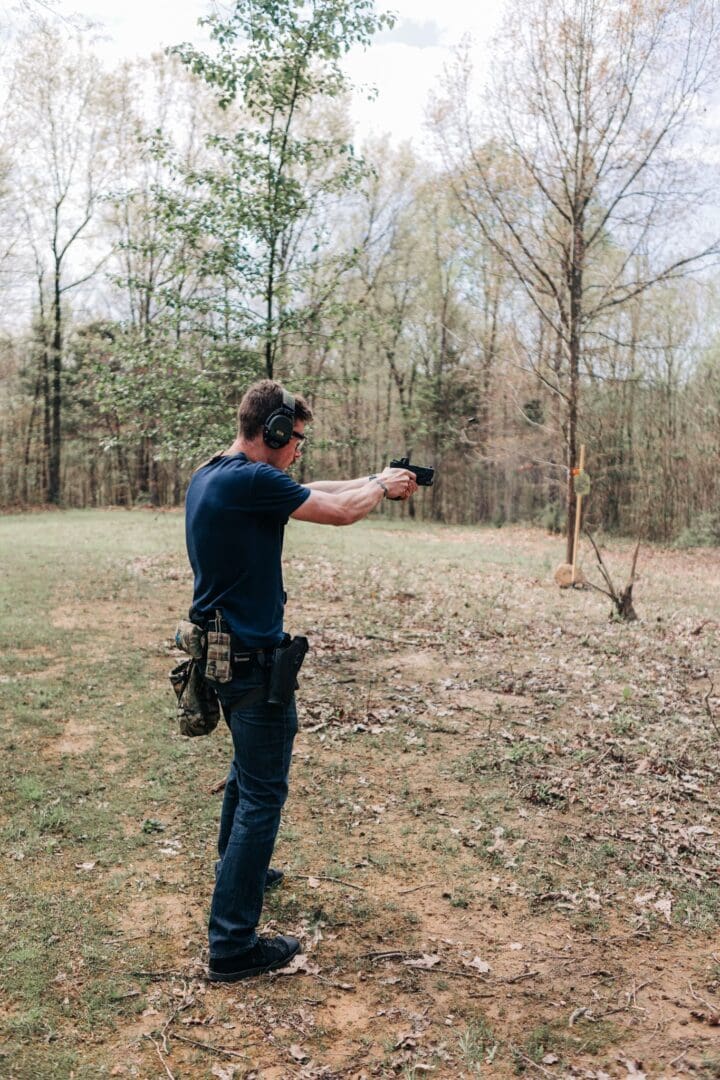 A man in blue shirt holding a gun near trees.