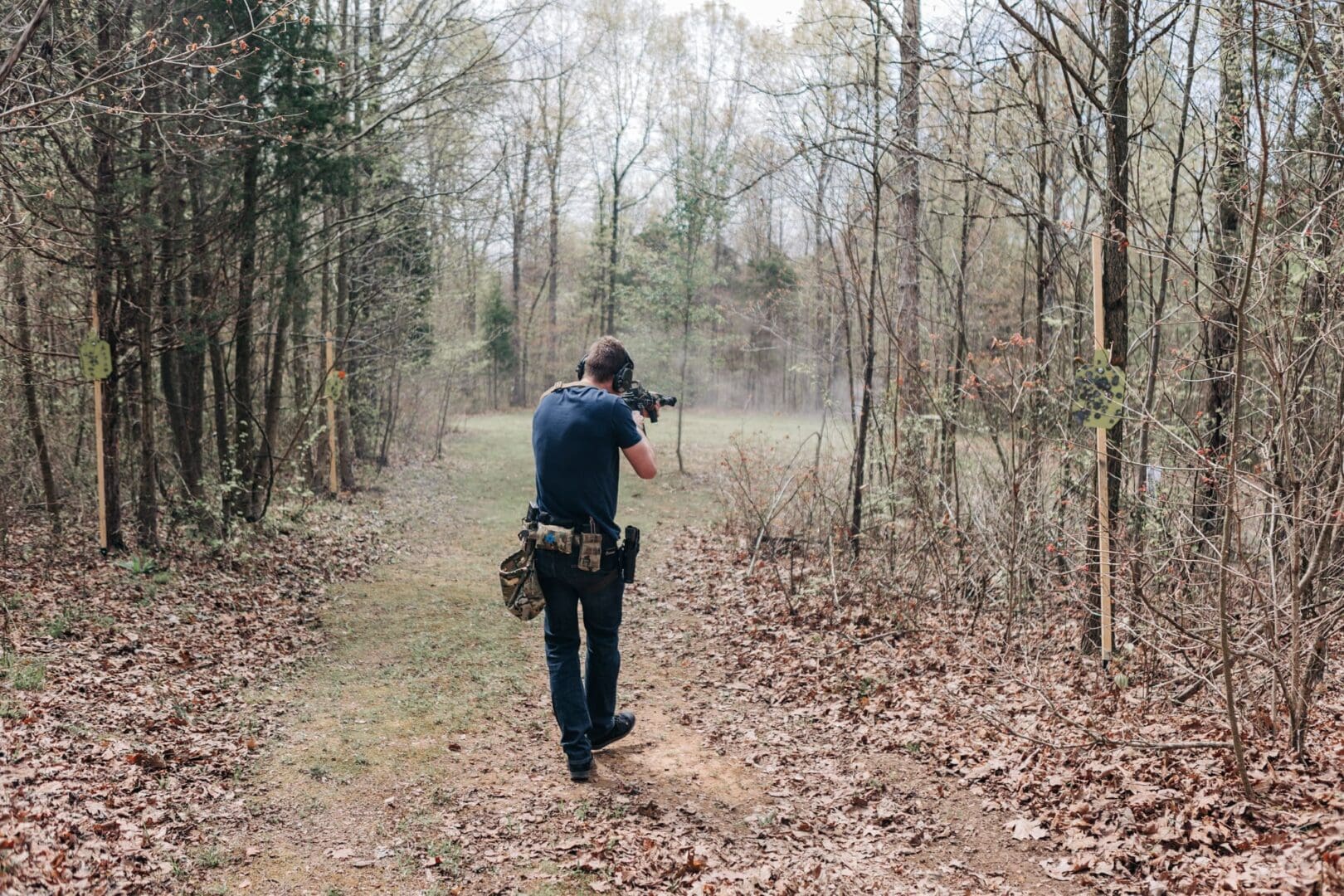 A man is standing in the woods with a rifle.