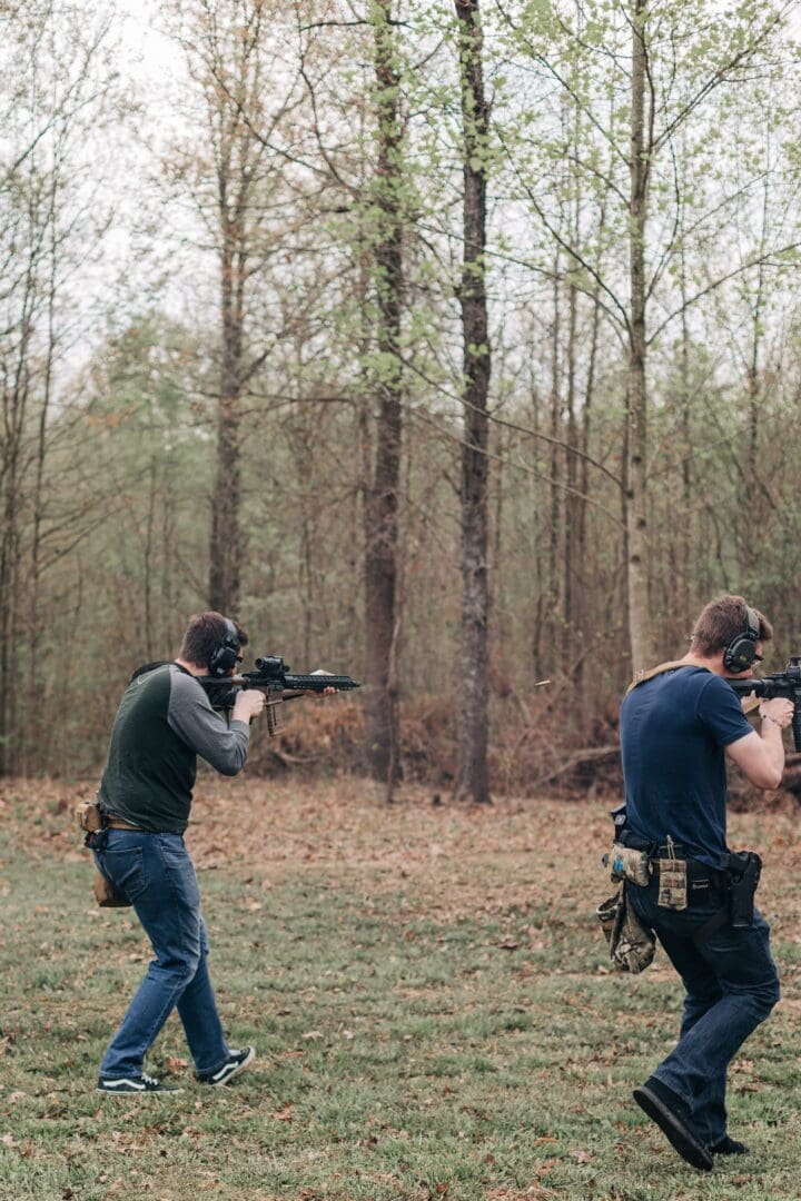 Two men are holding guns in the woods.