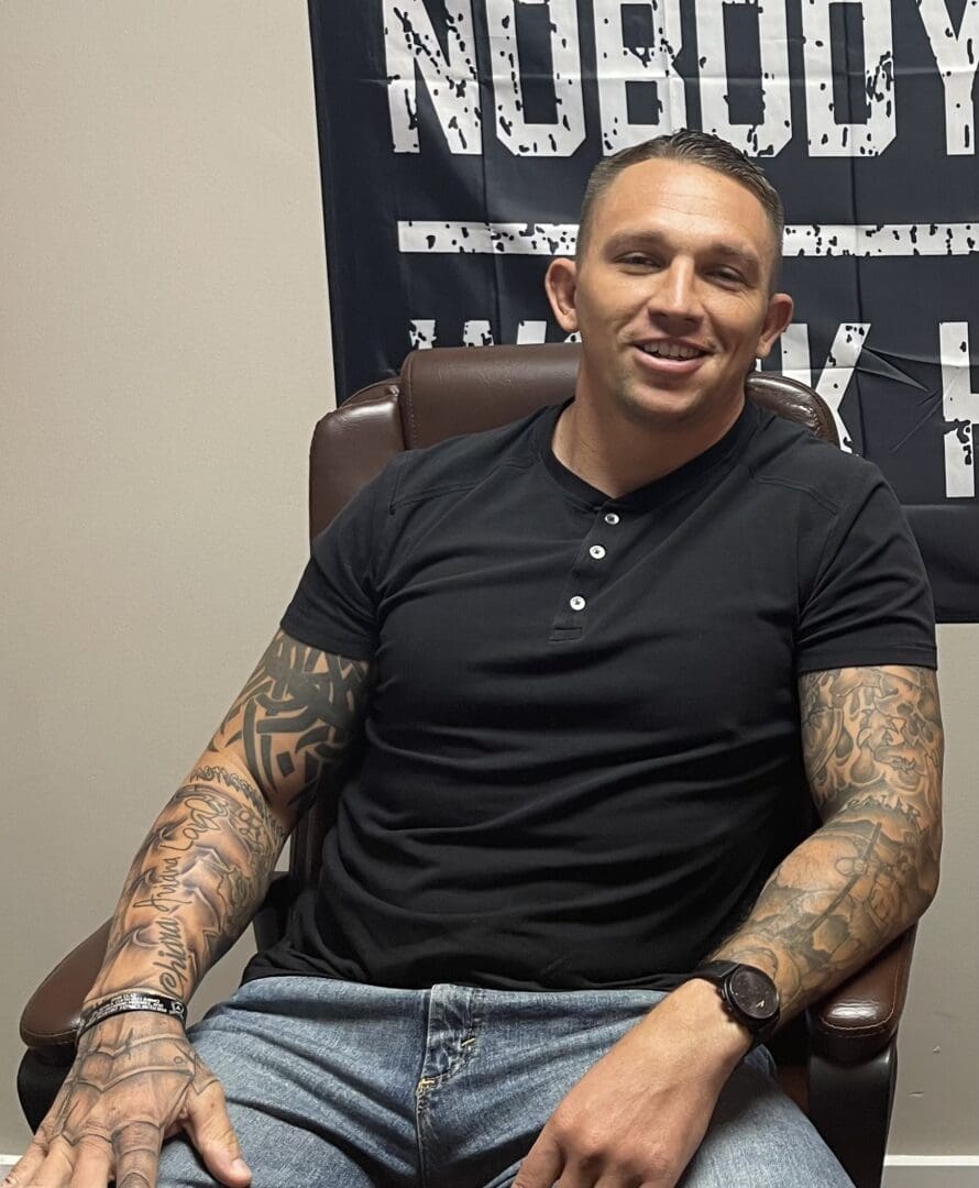 A man sitting in a chair with tattoos on his arms.