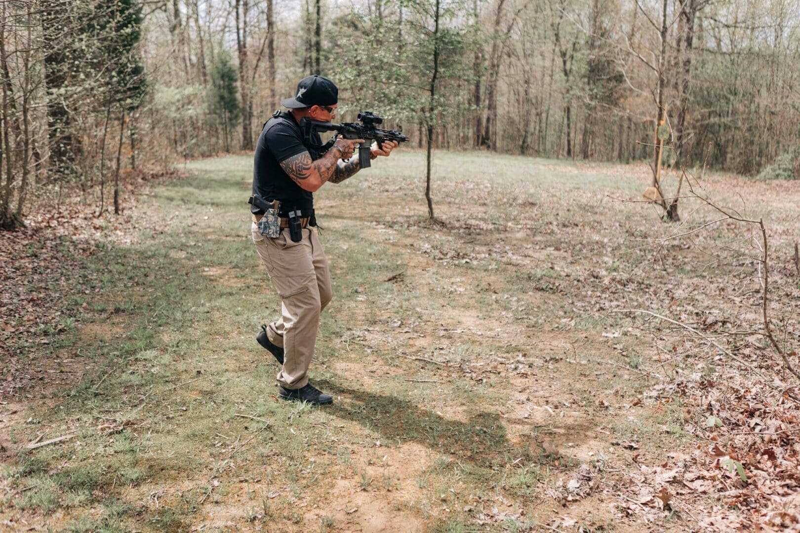 A man in black shirt holding gun near trees.