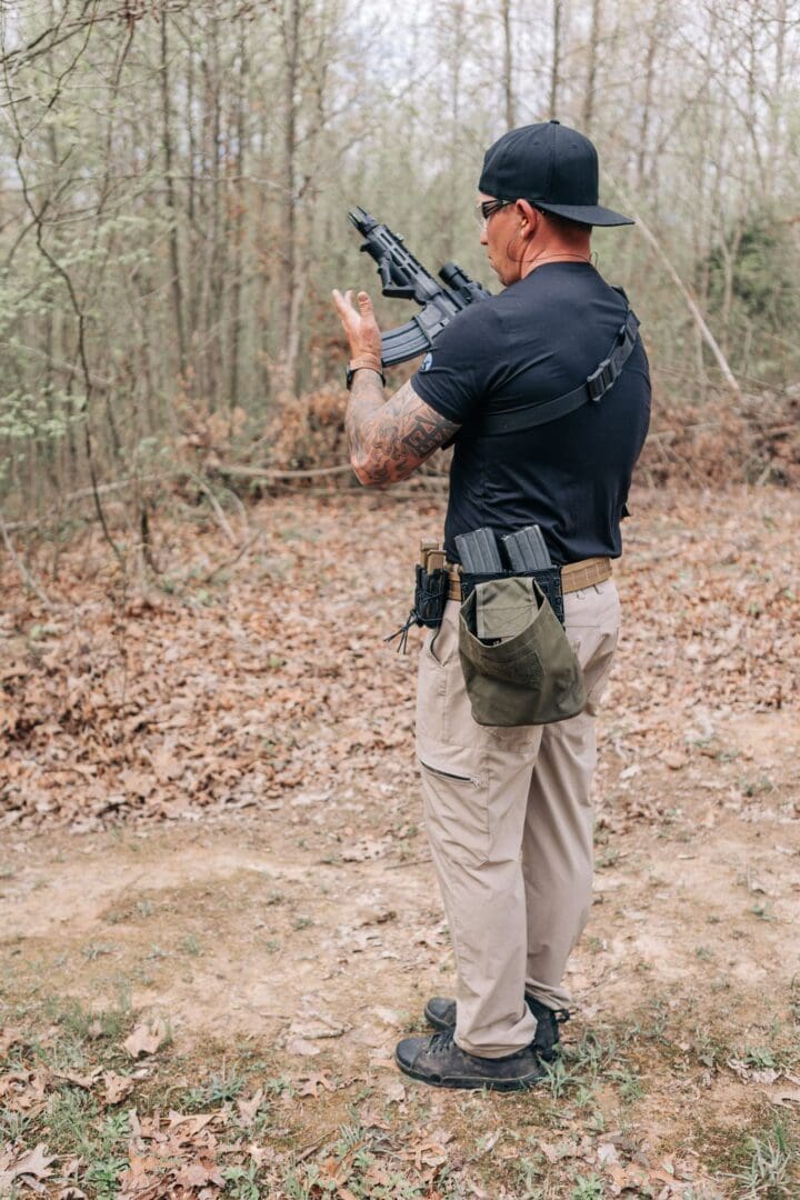 A man in black shirt holding a gun near trees.