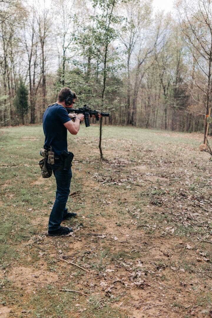 A man in blue shirt holding a rifle near trees.