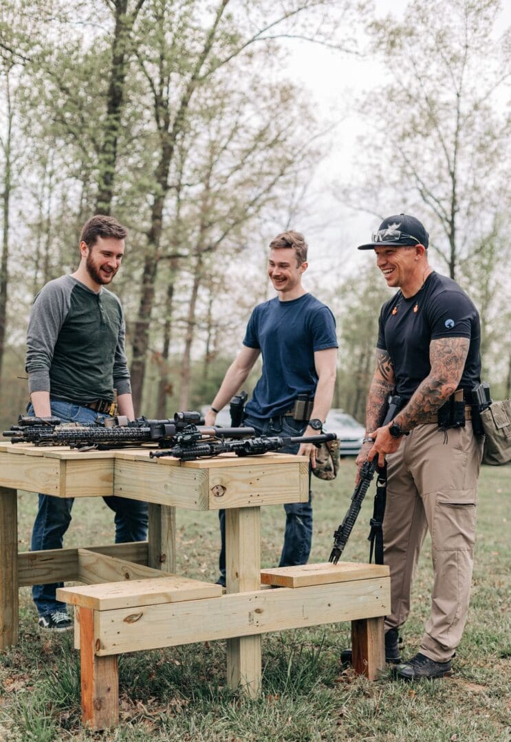 Three men standing around a wooden table with guns.