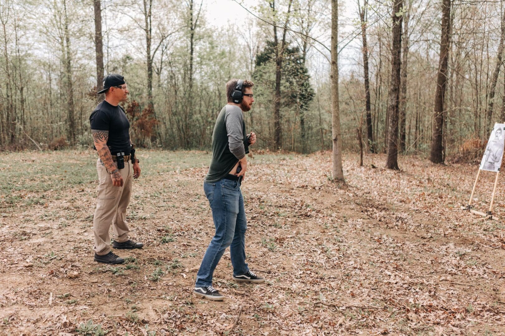 Two men standing in a wooded area holding guns.