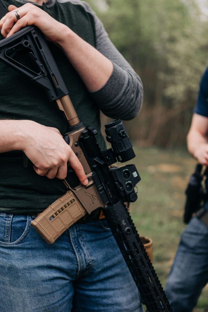 A man holding an ar-1 5 rifle while standing next to another man.