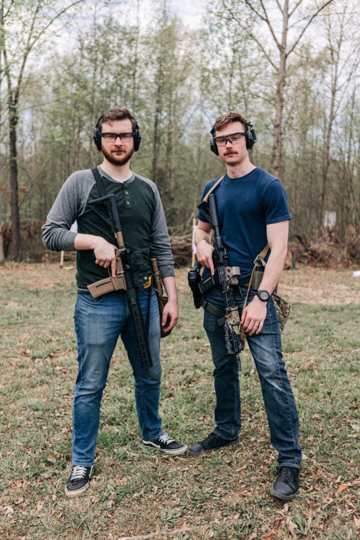 Two men standing in a field holding guns.