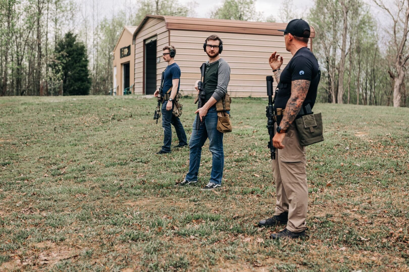 Three men in a field with guns and backpacks.