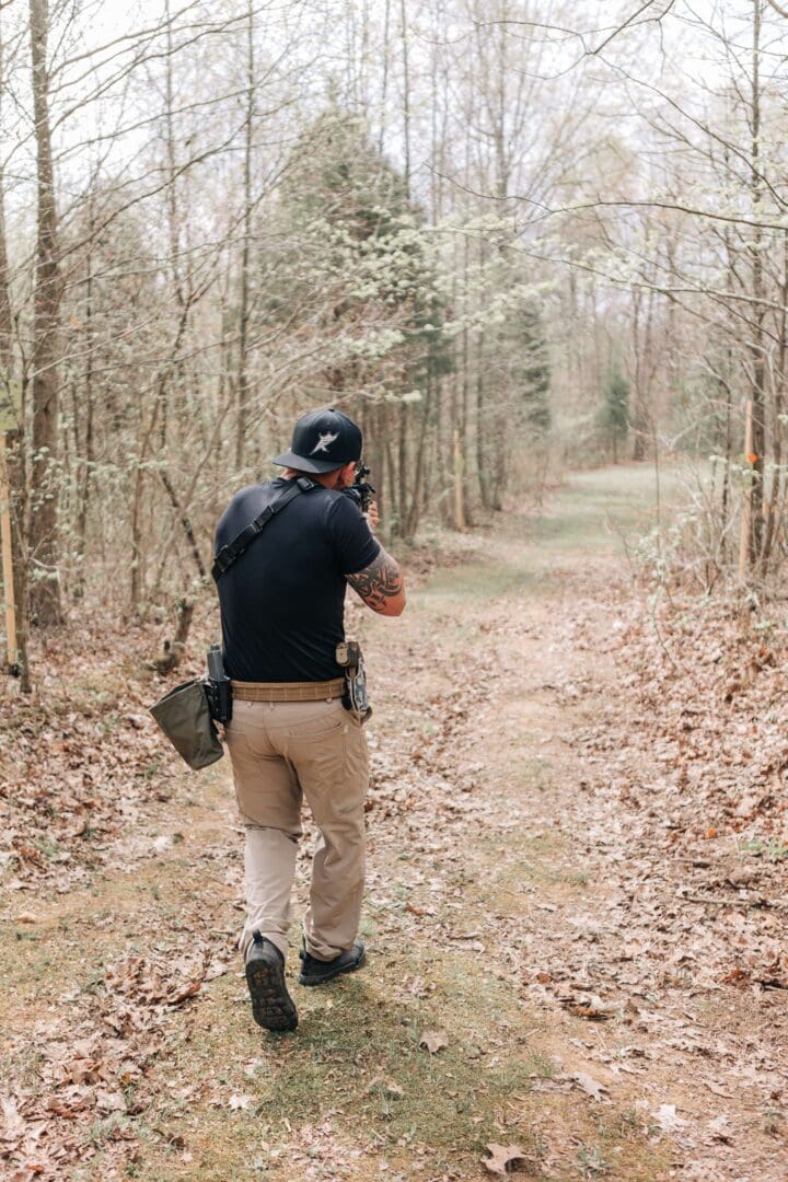 A man in black shirt standing on dirt road near trees.