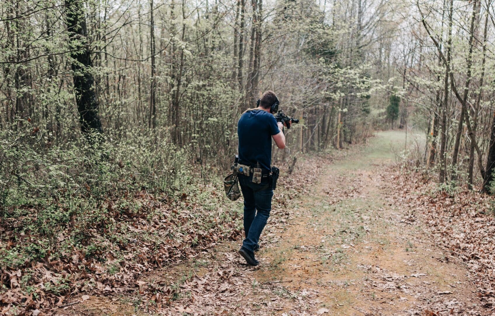 A man in blue shirt holding a camera near trees.