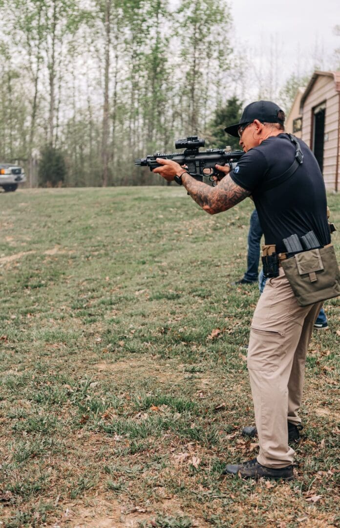 A man holding a gun while standing in the grass.