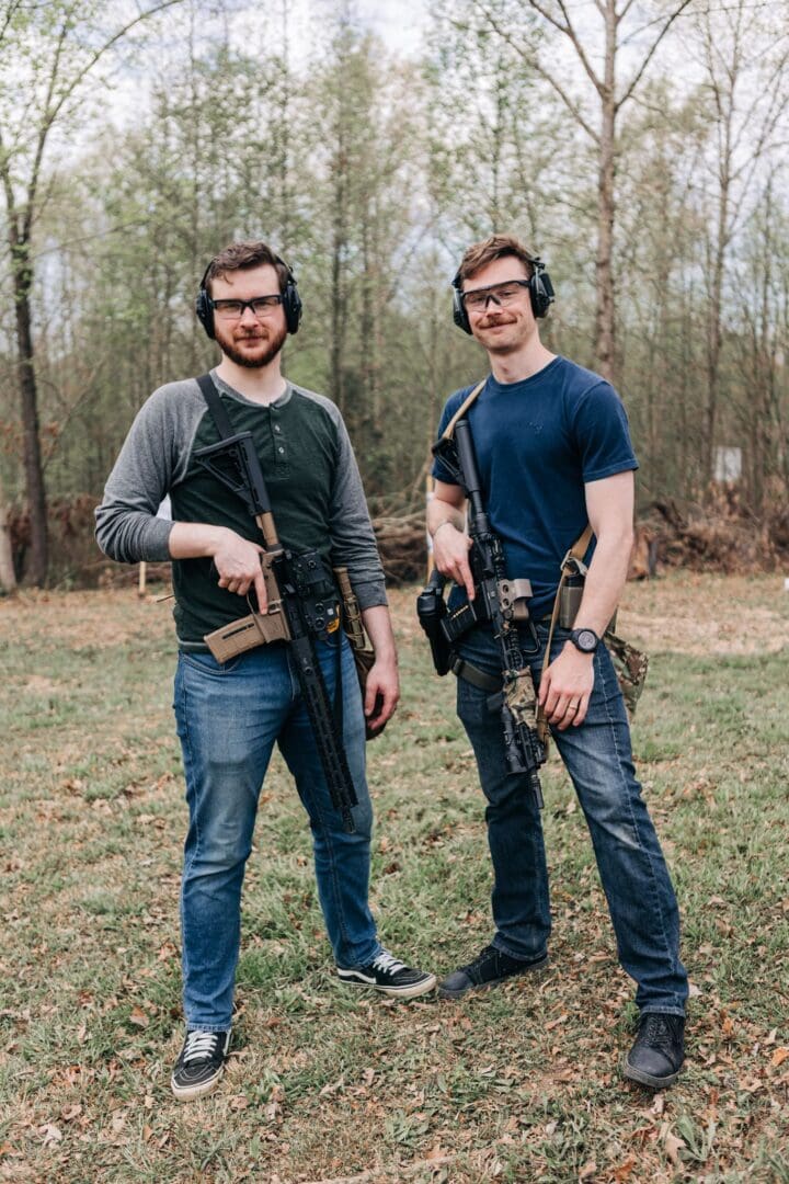 Two men standing next to each other holding guns.