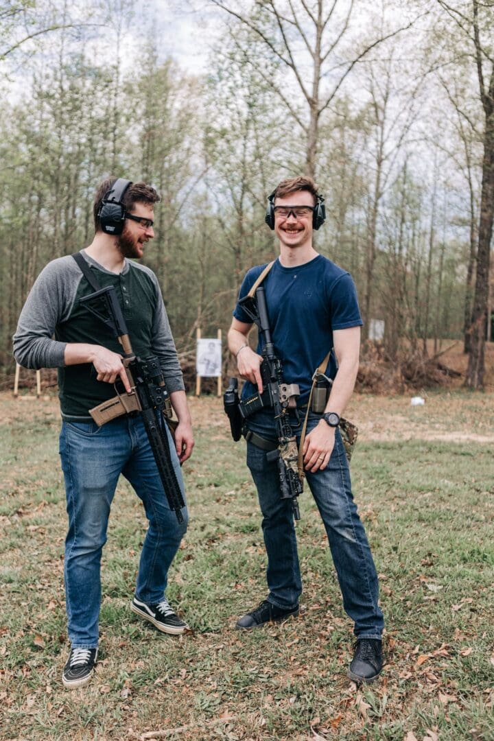 Two men standing next to each other holding guns.