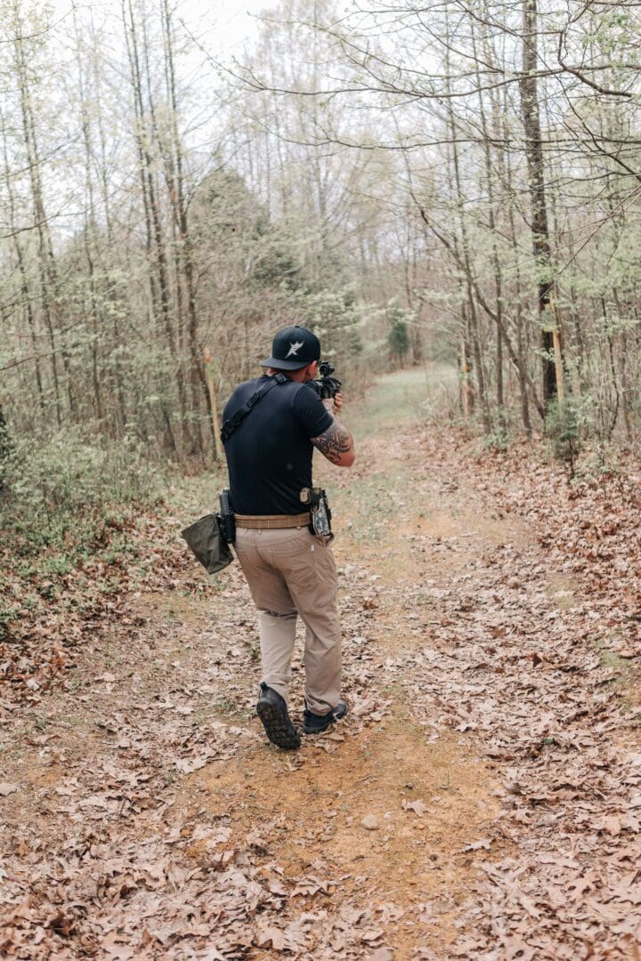 A man in black shirt standing on dirt road near trees.