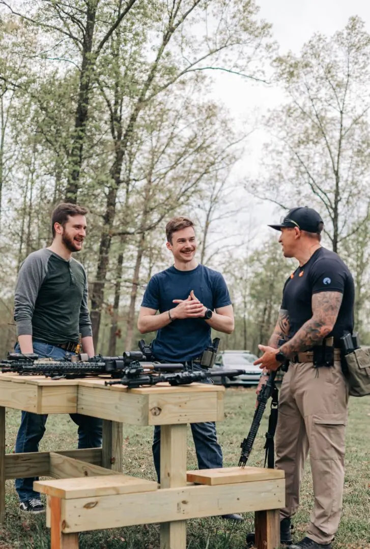 Three men standing around a table with guns on it.